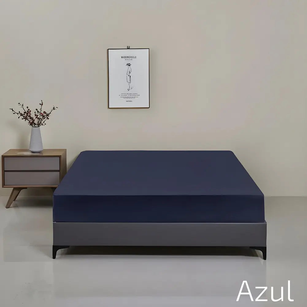 Imagem de uma cama com uma capa azul escura bem ajustada sobre o colchão, com base cinza escura. O fundo é uma parede bege com um quadro minimalista pendurado no centro. Ao lado da cama, um criado-mudo de madeira com um vaso cinza contendo ramos secos. O texto no canto inferior direito diz "Azul".